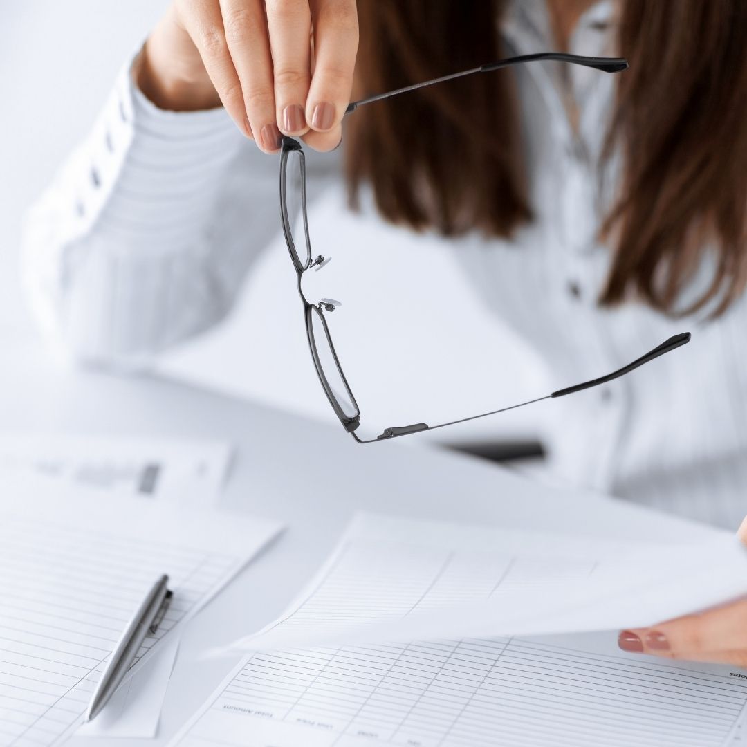 woman holding glasses over financial reports